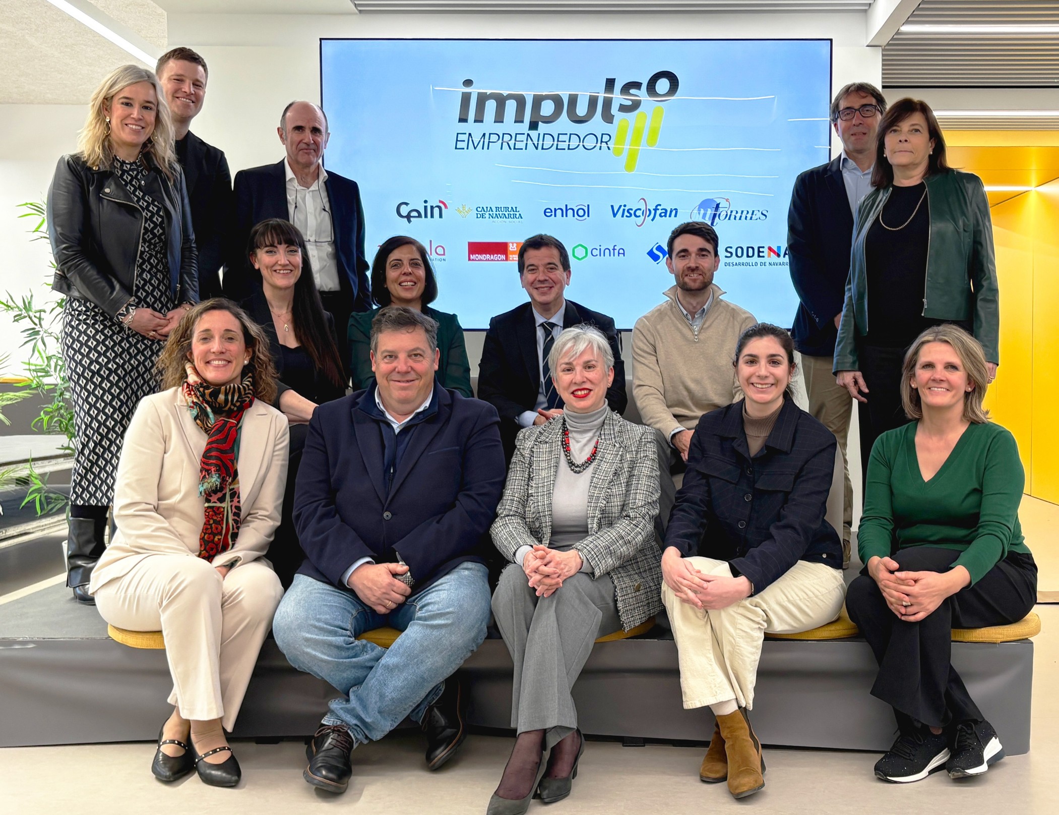 Foto grupal de varias personas sentadas y de pie delante del logo de la iniciativa