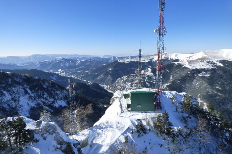 Fotografía de montes nevados con una torre eléctrica en la cima de uno de ellos