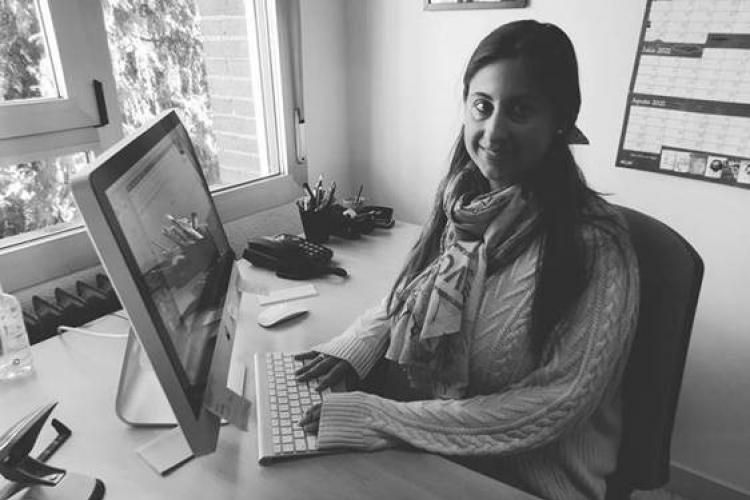 Fotografía en blanco y negro de Marina Muñoz, sentada delante del ordenador, sonriente y mirando a cámara.